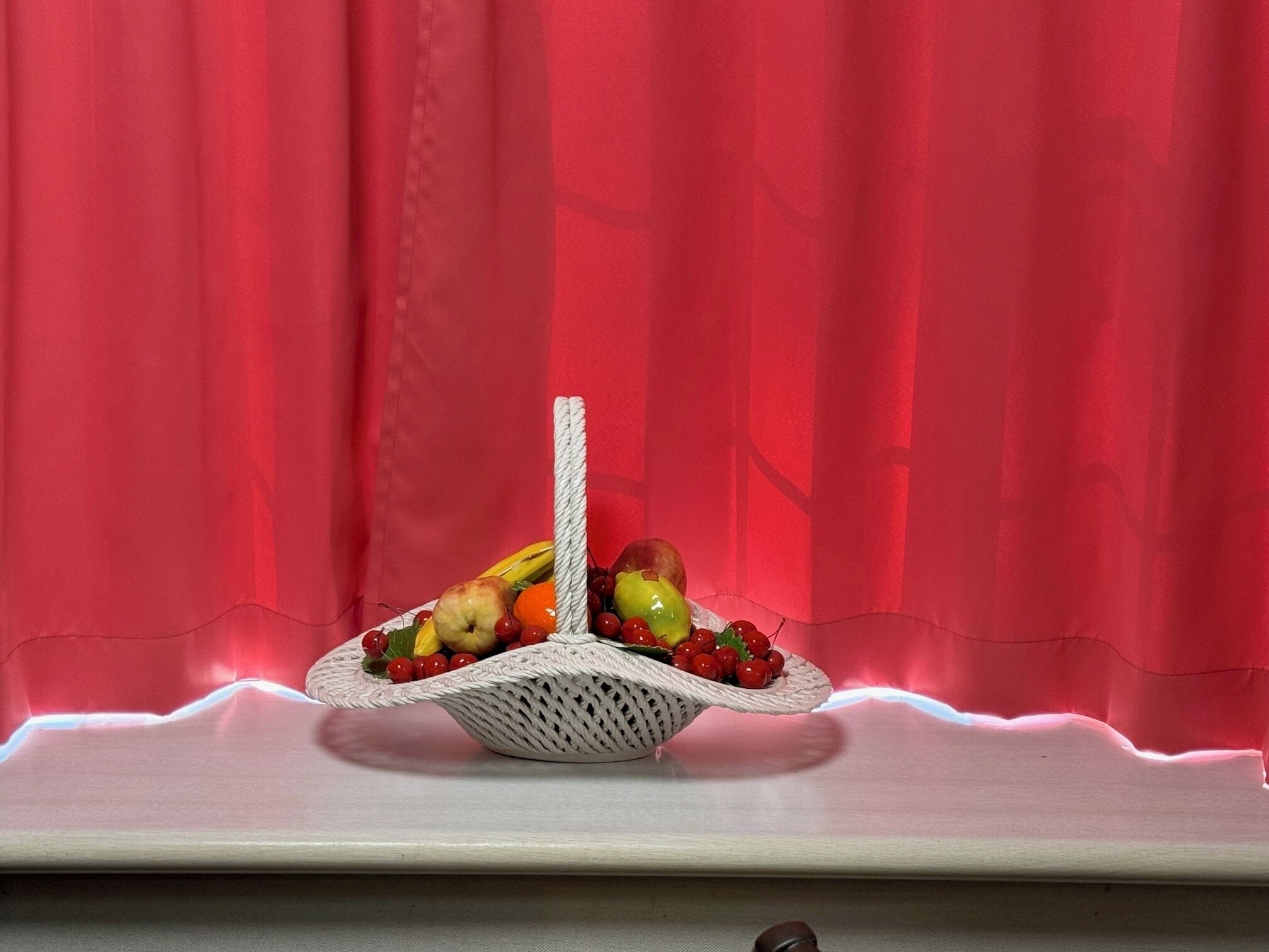 Ein Korbrand-Fruchtkorb auf einem Tisch mit rotem Vorhang im Hintergrund.