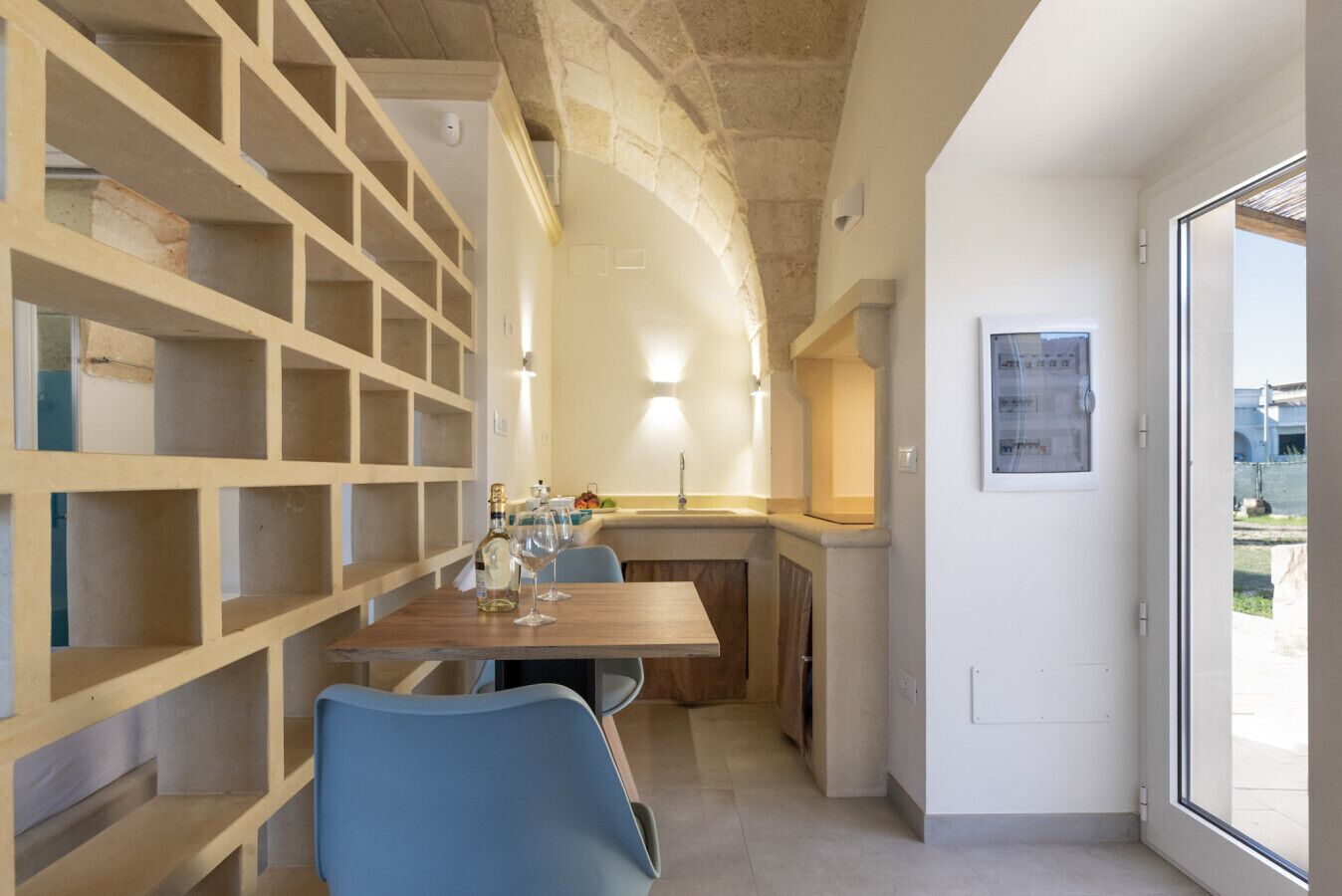 Una cucina moderna con isola integrata, zona pranzo con sedie blu e vista attraverso una porta in vetro.