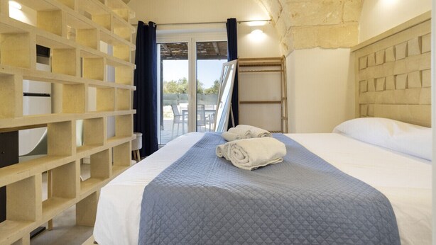 A hotel room with a bed, a wooden headboard, a built-in shelf unit, and a view of the outside. - Dimora Forticito - Marittima di Diso (Marittima)