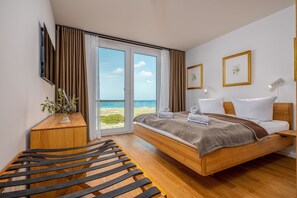A modern bedroom with a wooden bed, a small bedside table, a chair, and a view of the sea through a glass door. - Living and dreaming with a view of the Baltic Sea (Graal-Müritz)