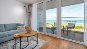 A modern living room with a sofa, a coffee table, and a view of the beach through large sliding glass doors. - Wonderfully modern vacation apartment with a direct view of the Baltic Sea (Graal-Müritz)