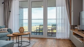 A modern living room with a large sliding glass door leading to a beach view, a cozy seating area with a small table, and a television on a wooden stand. - Wonderfully modern vacation apartment with a direct view of the Baltic Sea (Graal-Müritz)