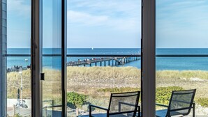 A view from a balcony with a glass door, overlooking a beach with a pier and people walking. - Wonderfully modern vacation apartment with a direct view of the Baltic Sea (Graal-Müritz)
