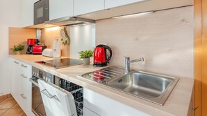 Uma cozinha moderna com armários brancos, uma pia de aço inoxidável, uma chaleira vermelha e um forno embutido.