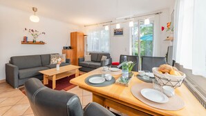 Uma sala de estar moderna com área de jantar, com um sofá, uma mesa de centro e uma mesa de jantar posta com pratos e uma cesta de pão.