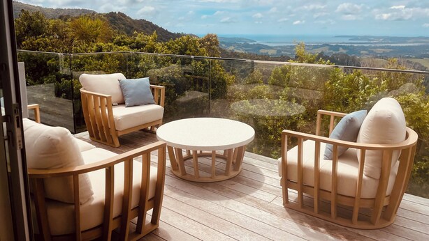 A balcony with wooden furniture, a glass barrier, and a view of a hilly landscape. - Matakana View- Treetop retreat in Matakana (Whangaripo)