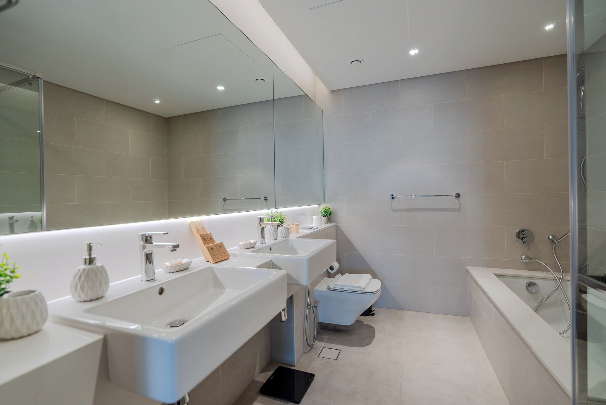 A modern bathroom with a large mirror, two sinks, a toilet, and a bathtub.