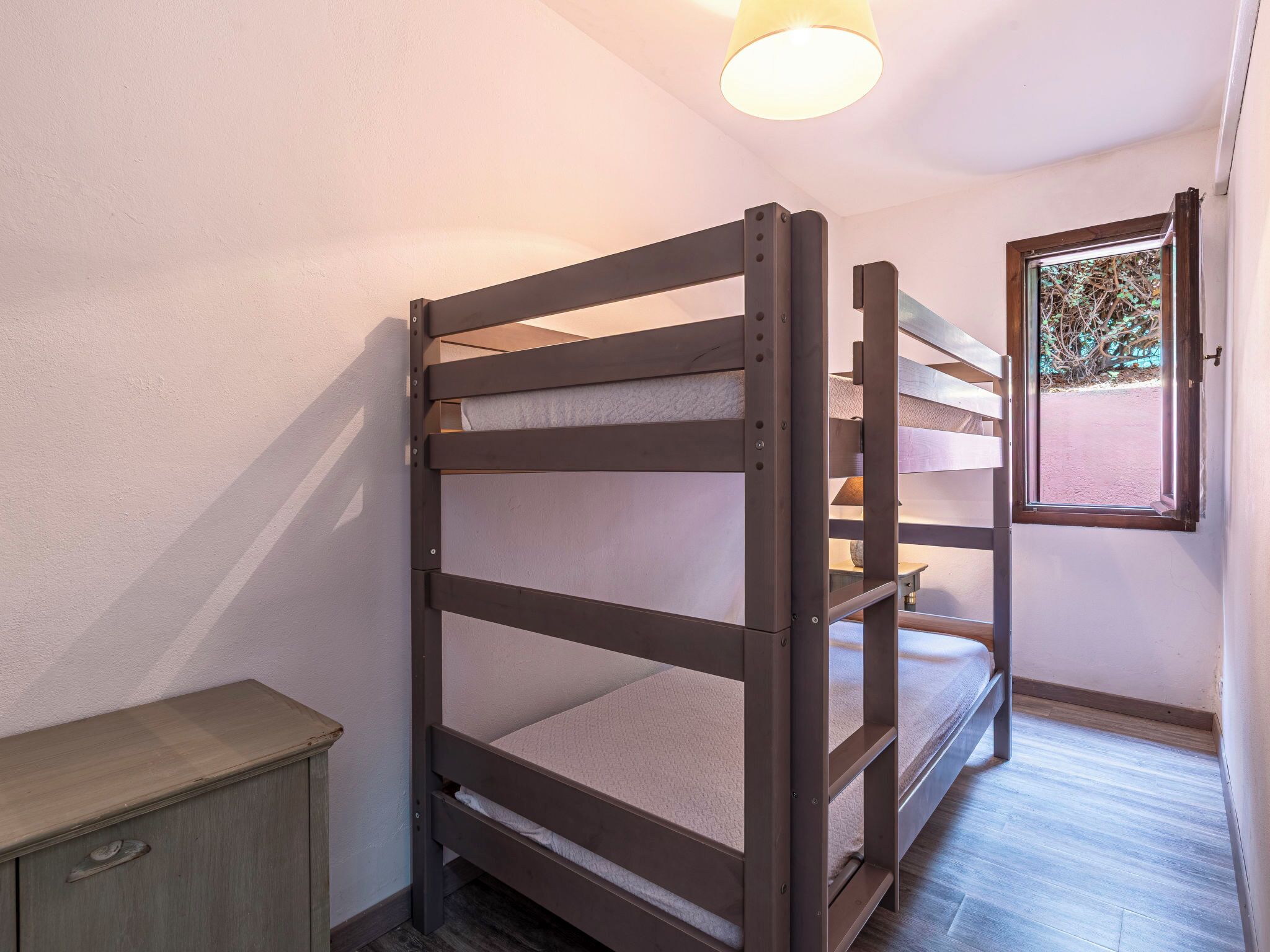 Un letto a castello con una finestra, un piccolo armadietto e una luce a soffitto.