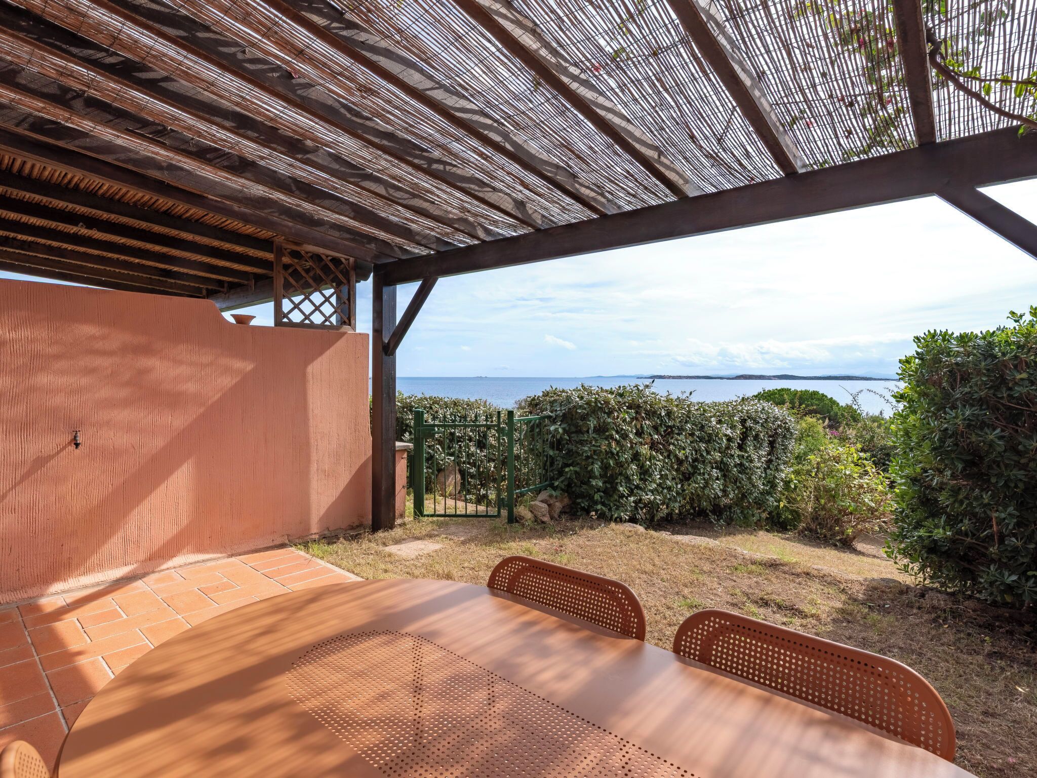A covered outdoor seating area with a table and chairs, overlooking a scenic view of the sea and distant land.