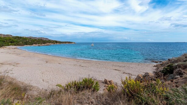 Ein Strand mit Segelboot, blauem Himmel und felsiger Küste.