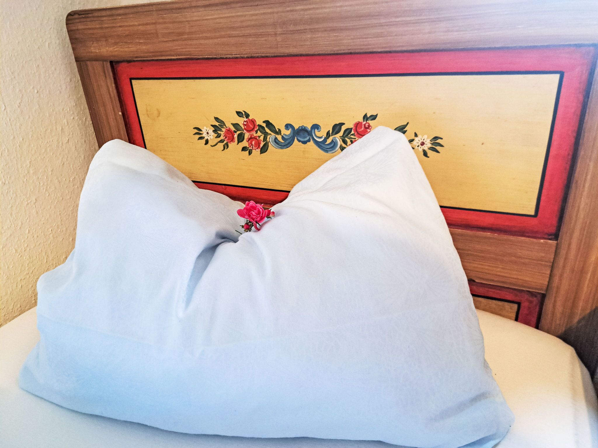 A white pillow with a floral design on a wooden headboard.