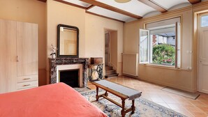 Une chambre à coucher avec un lit, un banc, une cheminée, un miroir et une vue sur l’extérieur.