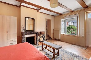 A bedroom with a bed, a bench, a fireplace, a mirror, and a view of the outside.