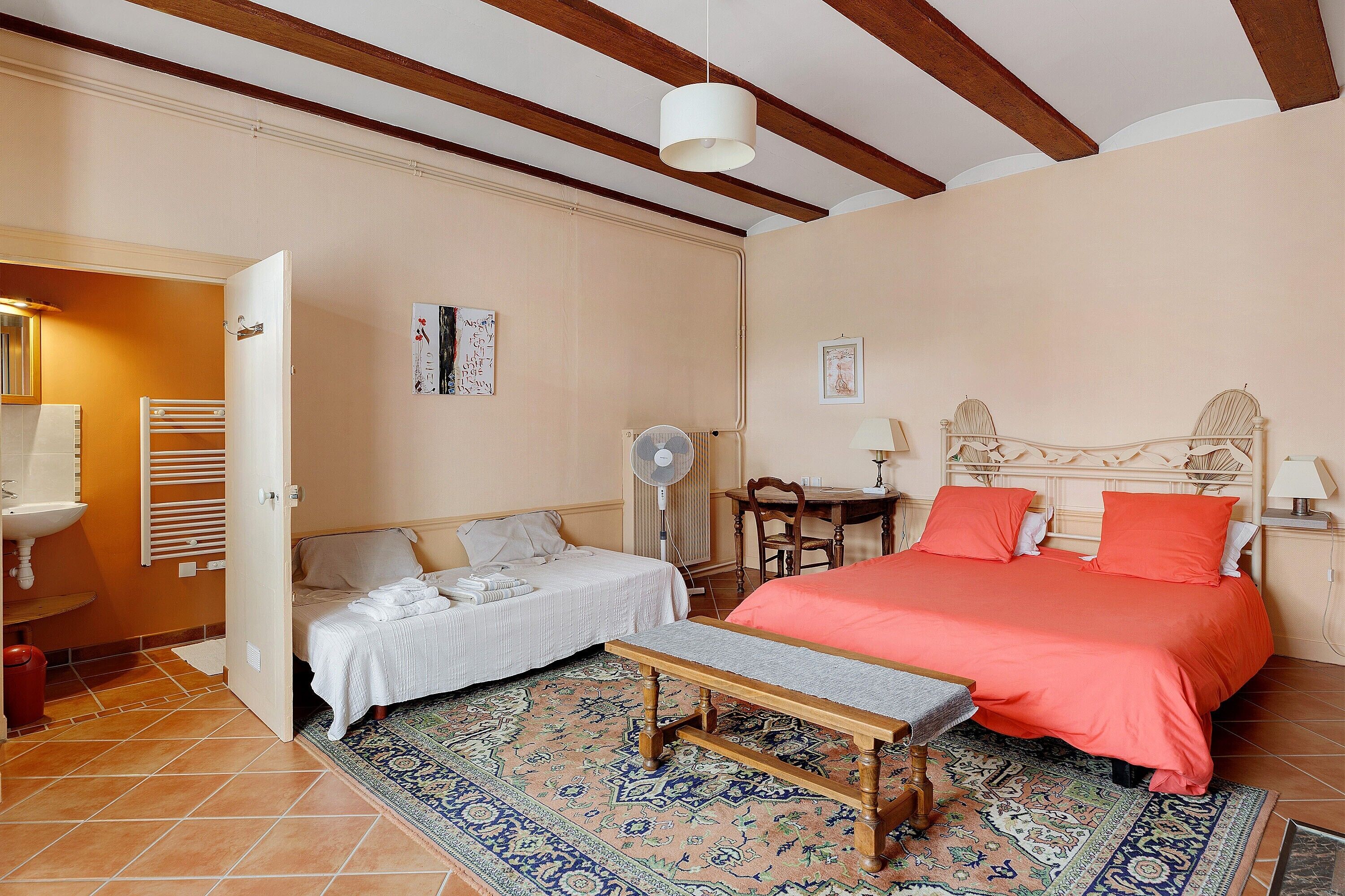 A bedroom with a bed, bedside table, chair, and a small table with a lamp.