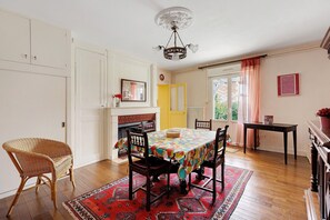 A dining area with a table, chairs, a wicker chair, a fireplace, and a view of the outdoors.