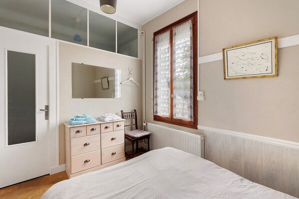 A bedroom with a bed, dresser, chair, window, and wall-mounted artwork.