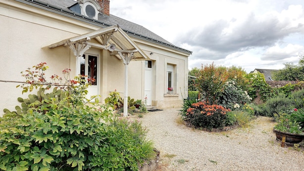 Une maison avec une allée en gravier, un jardin agrémenté de diverses plantes et fleurs, et une façade blanche.