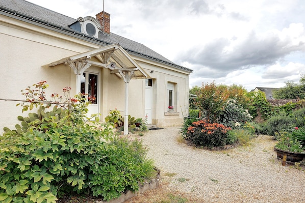 A house with a gravel driveway, a garden with various plants and flowers, and a white exterior.