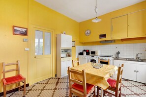 Uma cozinha com paredes amarelas, uma mesa de jantar com cadeiras, uma máquina de lavar e uma pia.
