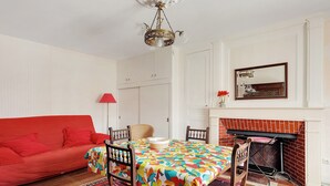 Un coin repas avec une table dressée pour quatre personnes, un canapé rouge, une cheminée et un lustre.