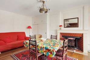 Un coin repas avec une table dressée pour quatre personnes, un canapé rouge, une cheminée et un lustre.