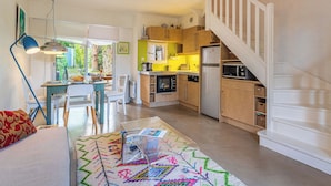 A spacious living area with a dining table, a sofa, and a colorful rug. There is a kitchen with modern appliances and a staircase leading to an upper level. - Les Parcs de Gassin by Interhome (Gassin)