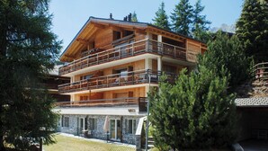 Un chalet en bois à plusieurs étages, doté de balcons et entouré d’arbres, sous un ciel dégagé.