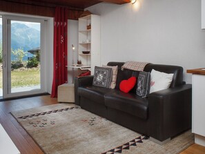 A living room with a black leather sofa, a red heart pillow, and a patterned throw blanket.