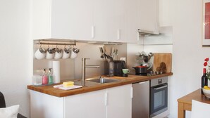 Une cuisine compacte avec des meubles blancs, un plan de travail en bois, un évier et un four encastré.