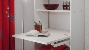 Un bureau blanc avec un livre ouvert, une lampe et un récipient en bois contenant des stylos.