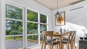 A dining area with a table and chairs, large windows with a view of greenery, and a hanging light fixture. - "Cornel" - 300m from the sea by Interhome (Strøby)