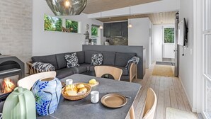 A modern kitchen with a stone backsplash, a dining area with a gray table and chairs, and a cozy seating area with a gray sofa and patterned cushions. - "Cornel" - 300m from the sea by Interhome (Strøby)