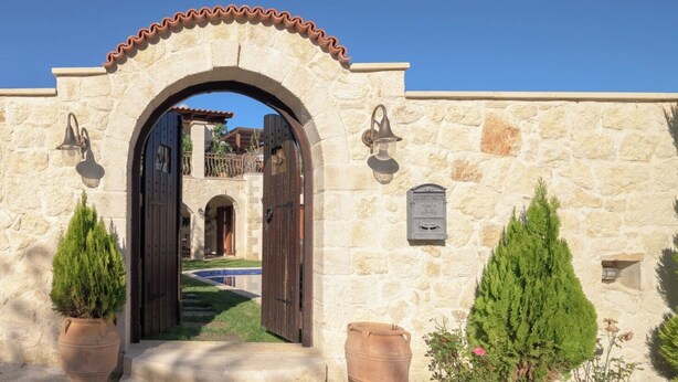 An arched stone entrance with a pool visible through the doorway, surrounded by potted plants and a mailbox. - Nicole Villa (Apokoronas)