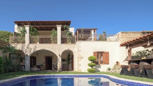 A poolside view of a Mediterranean-style villa with a tiled swimming pool, stone arches, and a balcony with plants. - Nicole Villa (Apokoronas)