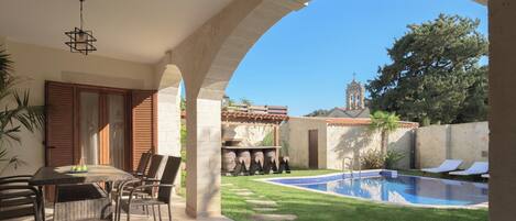 A covered patio with a pool, outdoor furniture, and a view of a church tower.