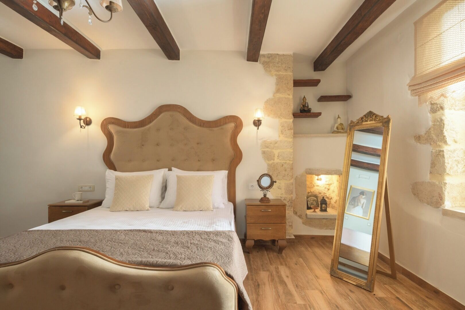 A bedroom with a large bed, wooden headboard, bedside tables, a mirror, and a stone wall.