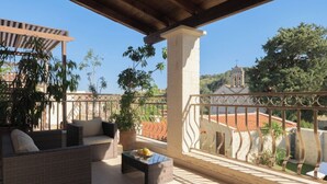 A covered outdoor seating area with wicker furniture and a glass coffee table, overlooking a church and greenery. - Nicole Villa (Apokoronas)