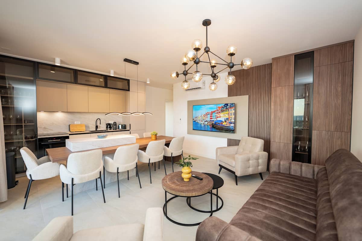 A modern living room with a brown sofa, a round coffee table, and a dining area with a wooden table and chairs.