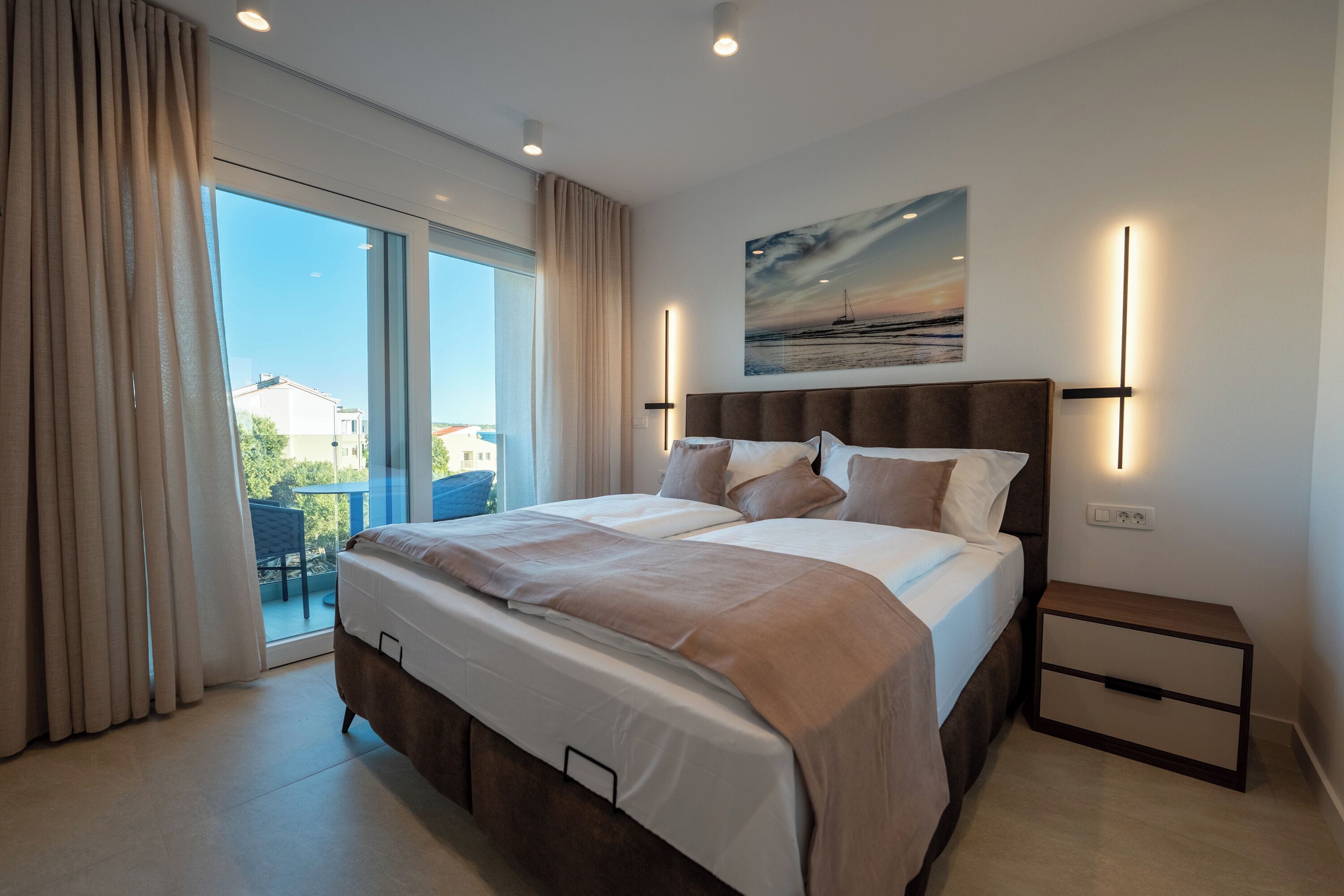 Un dormitorio moderno con una cama grande, una mesita de noche y vistas al exterior a través de una puerta corrediza de vidrio.