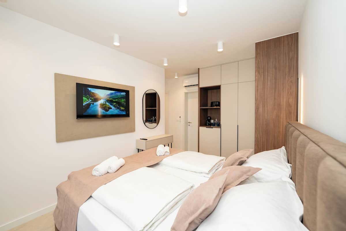 A modern hotel room with a bed, a TV mounted on the wall, a mirror, and built-in wardrobes.