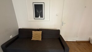 A dark-colored sofa with a single cushion against a white wall, a framed picture above it, and a closed door to the right.