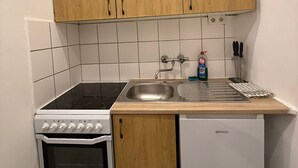 A compact kitchen with wooden cabinets, a built-in oven, a sink, and a dishwasher.