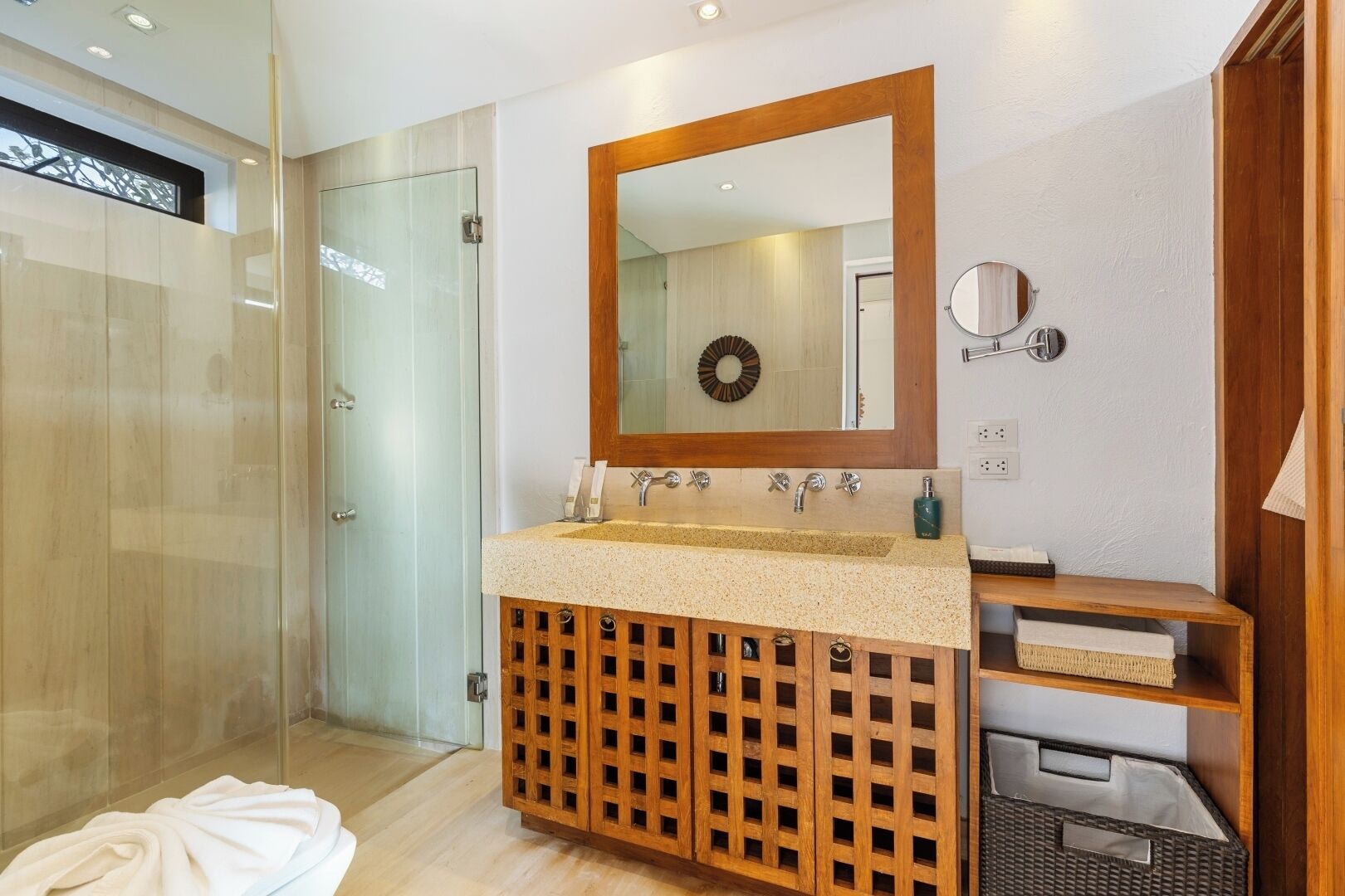 Une salle de bain moderne avec une douche à parois de verre, un meuble-lavabo en bois doté d’un grand miroir et un lavabo encastré.