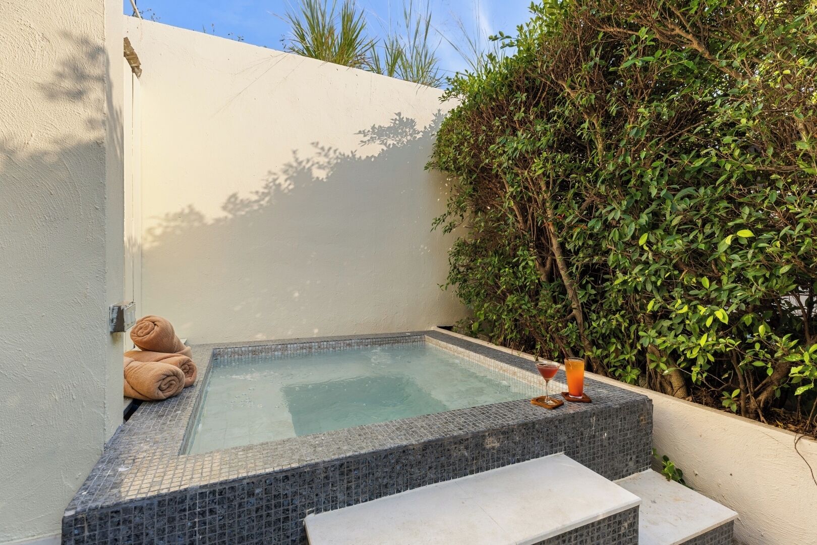 A hot tub with a tiled edge, a glass of drink, and towels on a ledge.