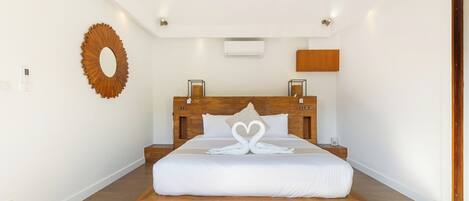 A modern bedroom with a wooden headboard, a large bed, a wall-mounted mirror, and a built-in air conditioning unit.