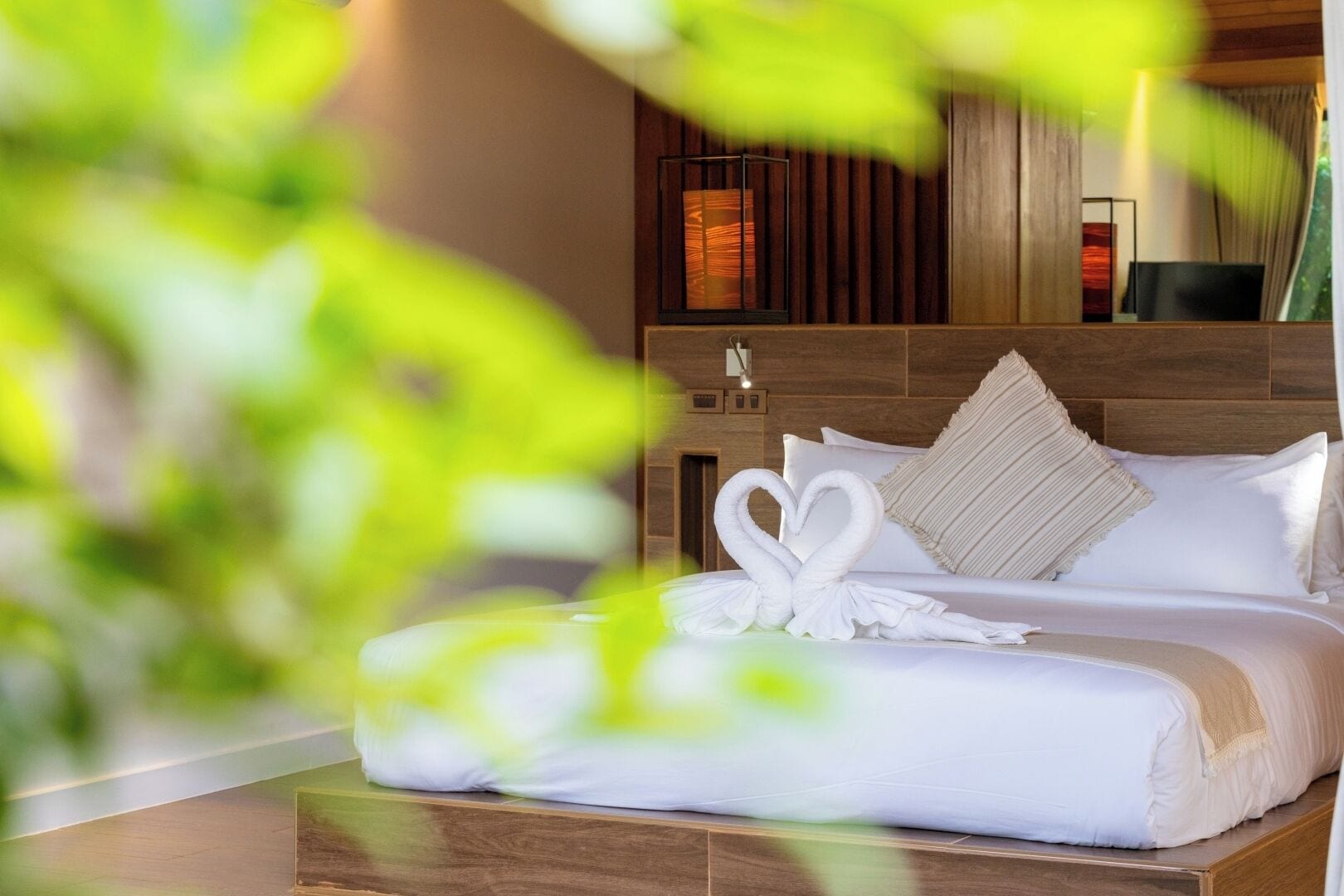 A hotel room with a wooden headboard, a bed with white bedding, and a heart-shaped towel decoration.