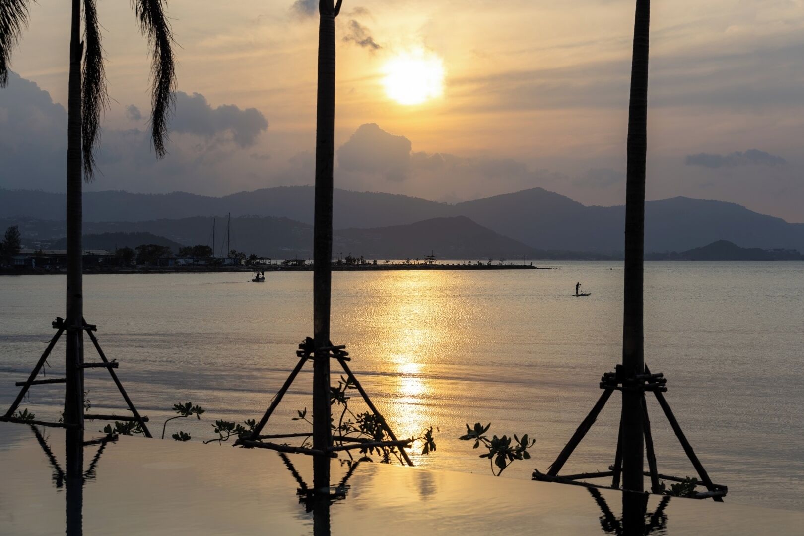 A sunset over a calm body of water with palm trees and a distant shoreline.