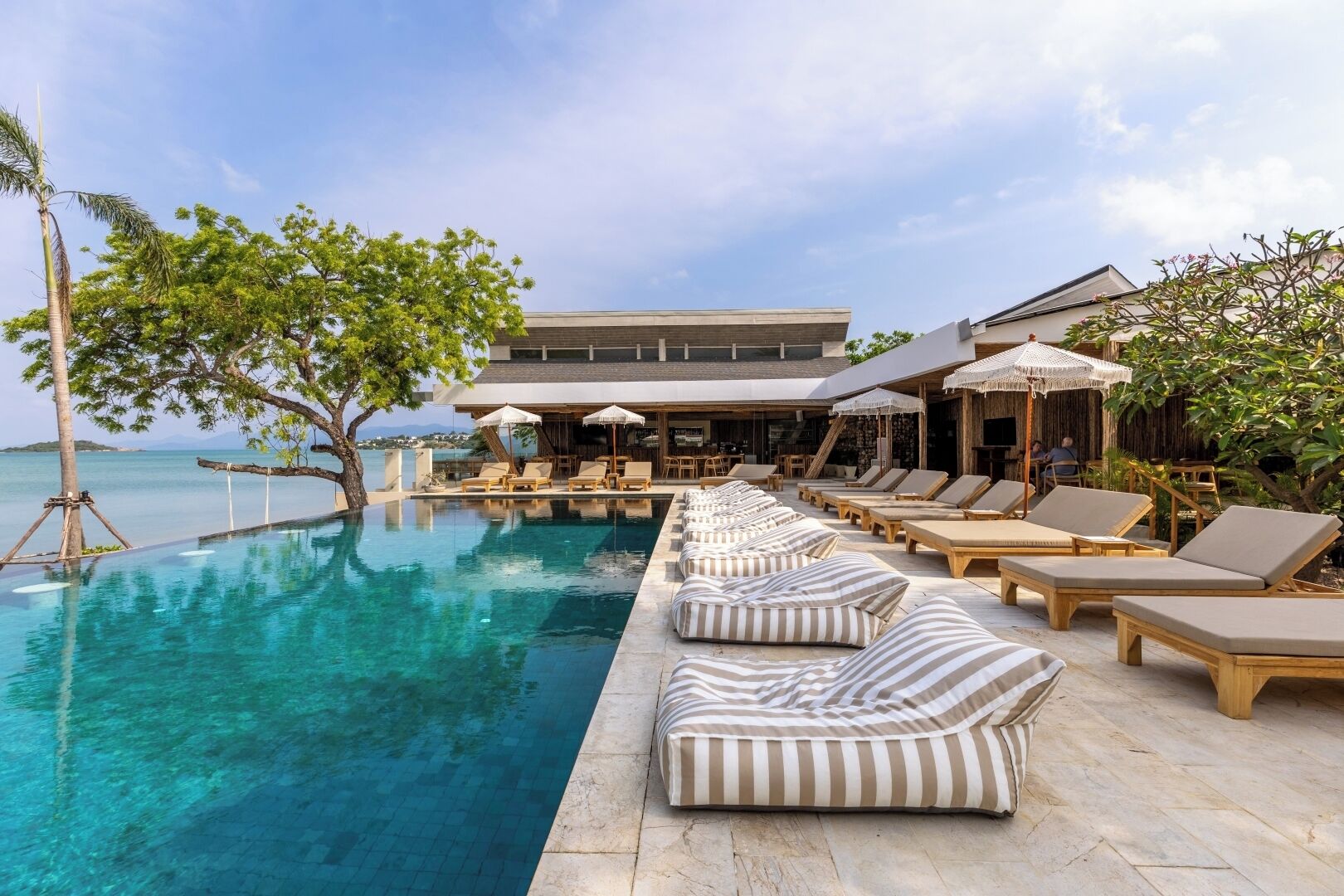 Un espace aménagé au bord de la piscine, avec des chaises longues, des parasols et un bâtiment en arrière-plan.