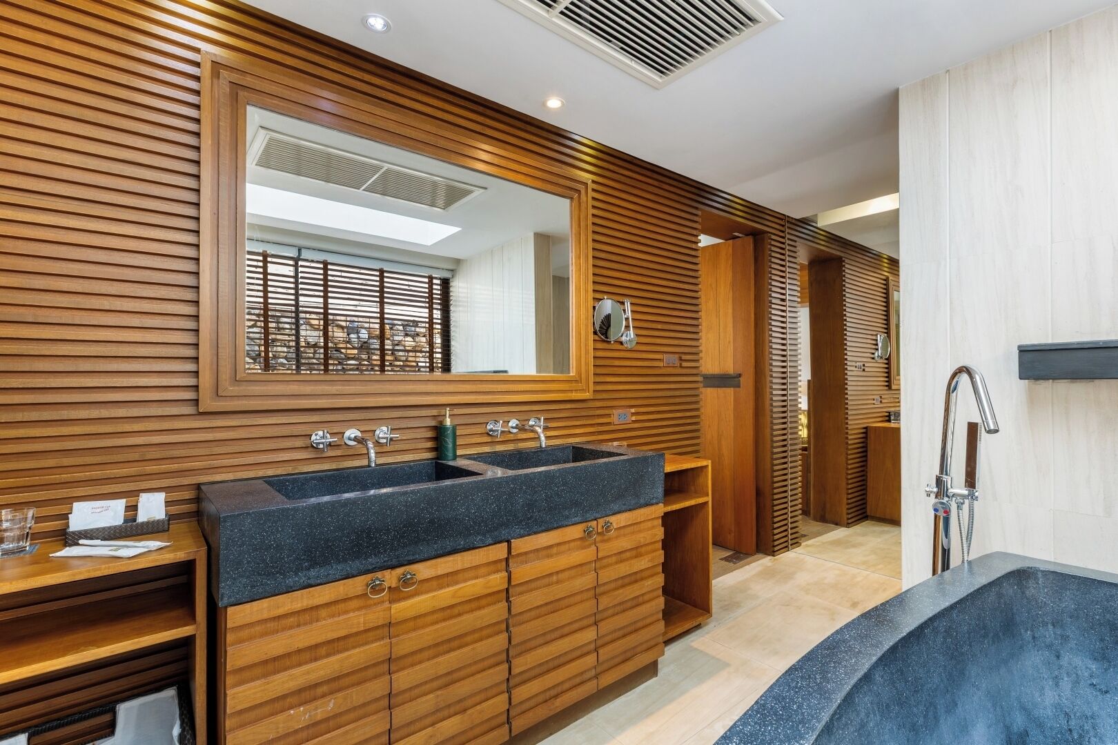 Une salle de bain moderne avec un lambris en bois, un grand miroir, un double vasque et un espace douche.