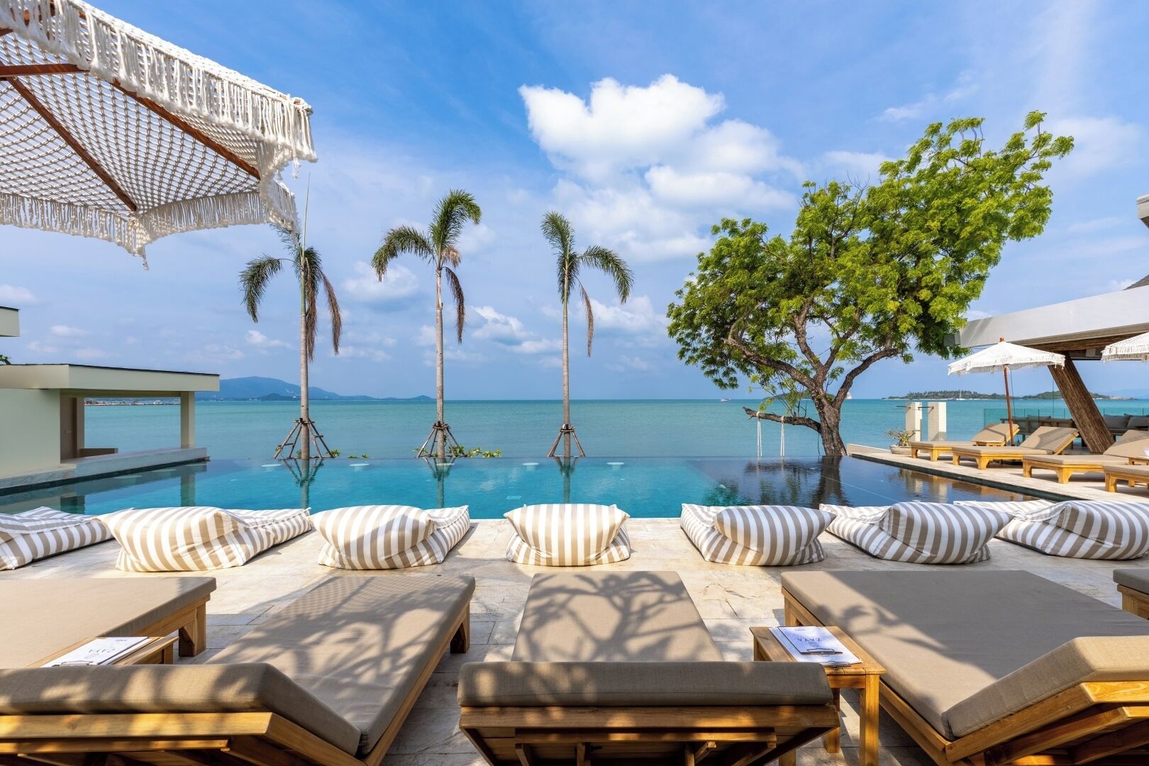 A poolside lounge area with sun loungers, striped pillows, and a view of the ocean.